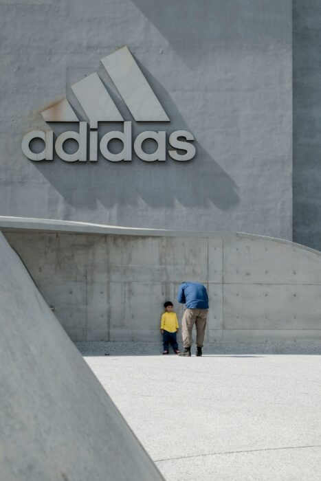 Adulte prenant en photo un enfant devant logo Adidas en ciment
